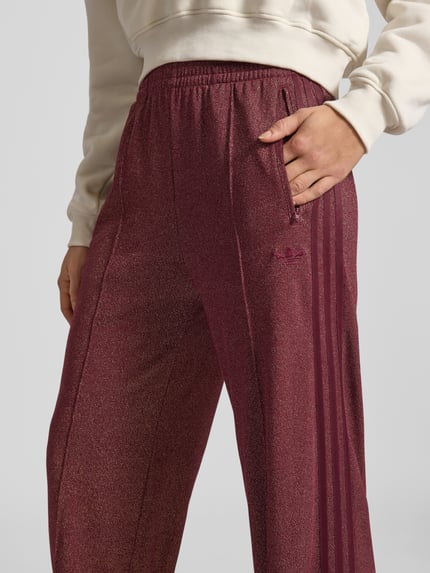 Vrouwenmodel draagt Sweatpants met elastisch bund van adidas Originals, katoenmix, los model, glittereffect, ritszakken, labelstitching, binnenbeenlengte maat S 81 cm. Detailopname.