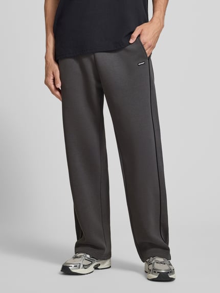 Männermodel trägt Straight Fit Sweatpants aus reiner Baumwolle mit Label-Patch von REVIEW, dunkles Grau, glatte Textur, Nahaufnahme Oberkörper, Herren Sweatpants von REVIEW, elastischer Bund, Eingrifftaschen, Innenbeinlänge bei Größe M 40 cm.