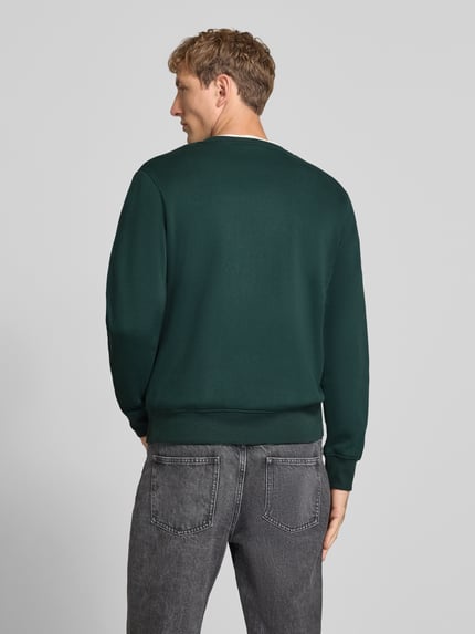 Mężczyzna nosi bluzę Sweatshirt mit Label-Print Model 'RUSH' od JACK & JONES, mieszanka bawełny, luźny krój, okrągły dekolt, prążkowane wykończenia, długość tyłu w rozmiarze M: 67 cm, długość rękawów w rozmiarze M: 67 cm, ciemnozielona, gładka tekstura, widok całej sylwetki z tyłu.