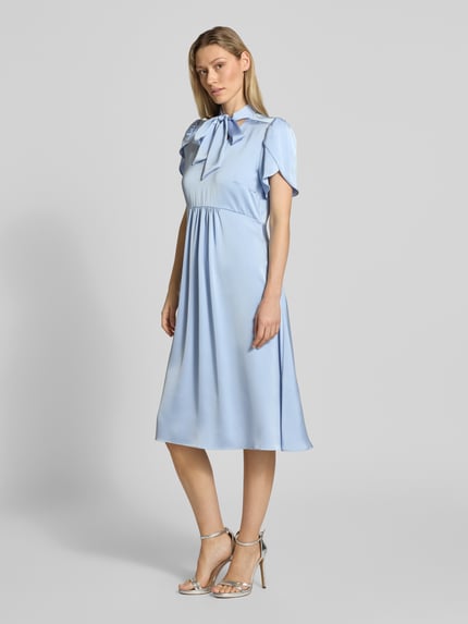 Vrouwenmodel draagt lichtblauwe midi-jurk met V-hals en strik van satijn in A-lijn met vlindermouwen van Christian Berg Woman Selection, ruglengte maat 36: 111 cm, borstwijdte maat 36: 46 cm, zijwaartse naadritssluiting, geheel lichaamsaanzicht van voren.