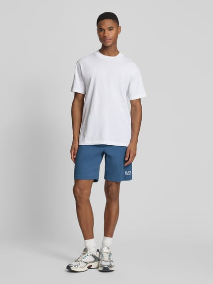Männermodel trägt Sweatshorts mit Logo und Eingrifftaschen von EA7 Emporio Armani aus reiner Baumwolle, Regular-Fit, Ganzkörperansicht von vorne.