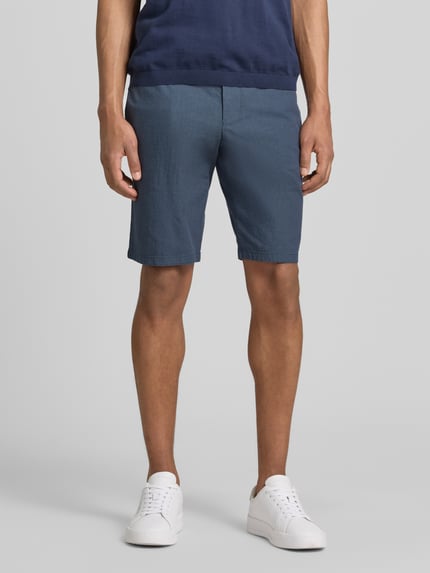 Männermodel trägt Bermudas mit Gürtel und Gesäßleistentaschen von Christian Berg Men aus Baumwoll-Mix mit Stretch-Anteil, Straight Fit, Knopf- und Reißverschluss, französischen Eingrifftaschen, Bundweite bei Größe 50: 45 cm, Innenbeinlänge 28 cm, Ganzkörperansicht von vorne.