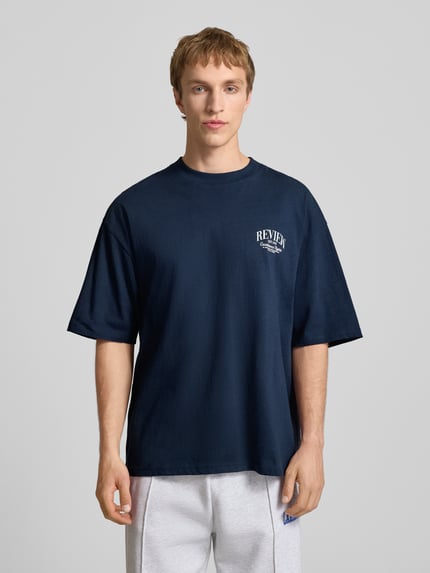 Männermodel trägt T-Shirt mit Label-Detail von REVIEW, dunkelblau, Reine Baumwolle, Lockerer-Schnitt, Rundhalsausschnitt, 1/2-Arm, Rückenlänge bei Größe M 68 cm, Ganzkörperansicht von vorne.