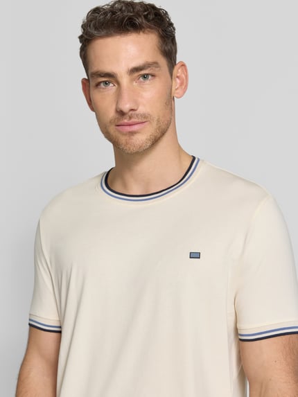 Männermodel trägt T-Shirt mit Kontraststreifen und Rundhalsausschnitt von Christian Berg Men aus Baumwoll-Elasthan-Mix, Regular-Fit, Nahaufnahme Oberkörper. Rückenlänge bei Größe M: 71 cm, cremefarbene glatte Oberfläche mit dezentem Label.