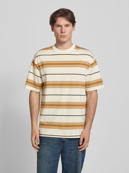 Männermodel trägt Oversized Shirt aus reiner Baumwolle Modell 'NIVARSI' von HUGO, gestreift in Beige und Braun, Ganzkörperansicht von vorne, Herren Oversized Shirt von HUGO Blue.
