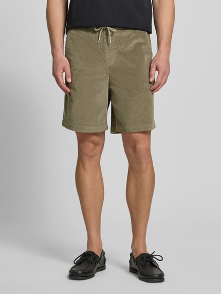 Męski model nosi Regular Fit Sweatshorts aus Baumwoll-Mix od SELECTED HOMME, bawełniany sztruks, jednolity, elastyczny pas, kieszenie, kolor oliwkowy, krój regular fit, zdjęcie całej sylwetki z przodu.