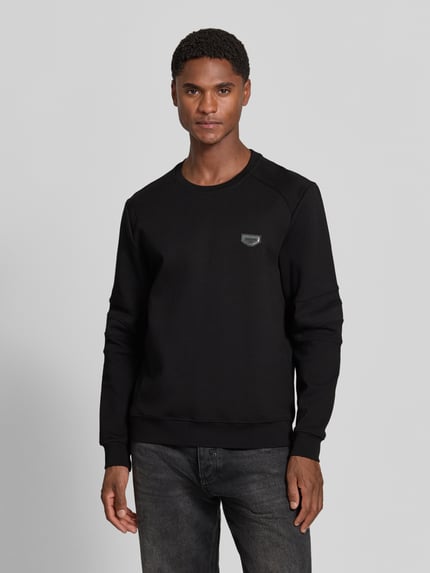 Männermodel trägt Sweatshirt mit Label-Patch Modell 'NEUTER' von Antony Morato in Schwarz, sichtbare Verstärkungen an Ärmeln, Ganzkörperansicht von vorne, taillierte Passform, gerippter Rundhalsausschnitt, elastische Abschlüsse, Kontext: Rückenlänge 66 cm, Ärmellänge 58 cm.