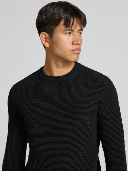 Männermodel trägt Regular Fit Strickpullover aus reiner Baumwolle von REVIEW in Schwarz mit gerippten Abschlüssen, Nahaufnahme Oberkörper.