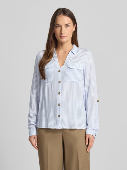 Frauenmodel trägt Relaxed Fit Hemdbluse aus reiner Viskose Modell 'BUMPY' von Vero Moda, hellblau-weiß gestreift, Ganzkörperansicht von vorne.