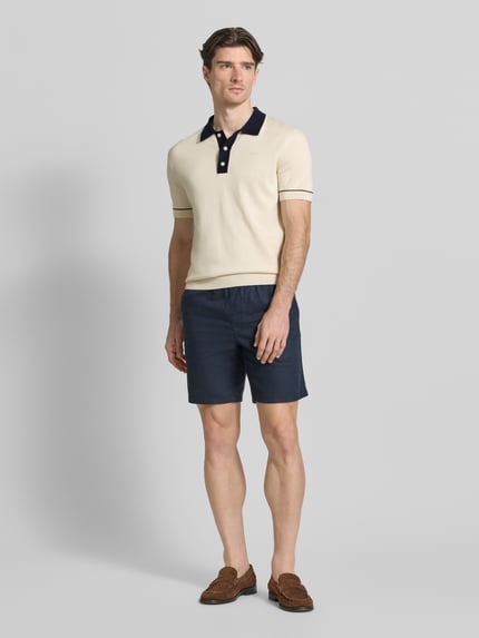 Männermodel trägt Slim Fit Poloshirt mit Logo-Stitching von Gant in Beige und Dunkelblau, Baumwoll-Modal-Mix, Ganzkörperansicht von vorne.