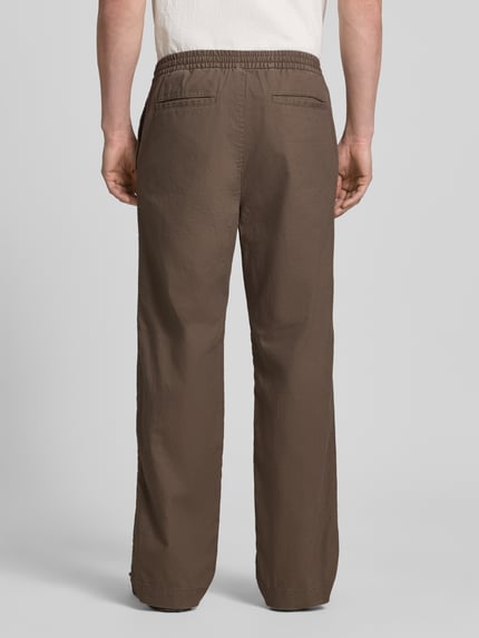 Männermodel trägt Leinenhose mit elastischem Bund und Eingrifftaschen von GAP in Braun, lockerer Schnitt, Ganzkörperansicht Rückansicht. Loose Fit im Leinen-Mix mit Baumwoll-Anteil, französische Eingrifftaschen, Gesäßleistentaschen, Bundweite bei Größe M 43 cm, Innenbeinlänge 80 cm.