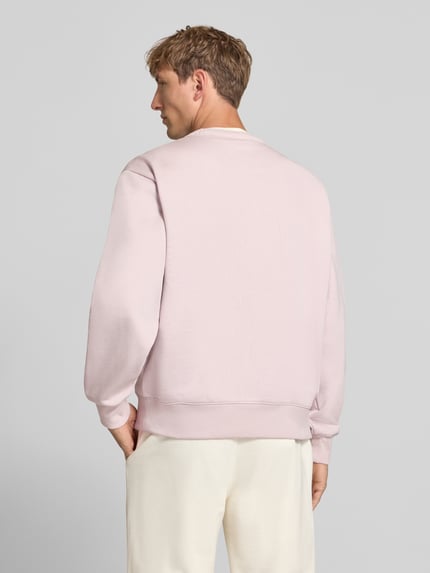Männermodel trägt Sweatshirt mit Label-Details von Champion in zartem Rosa aus Baumwoll-Mix, lockere Passform, Rückenansicht, Ganzkörperansicht Rückansicht.