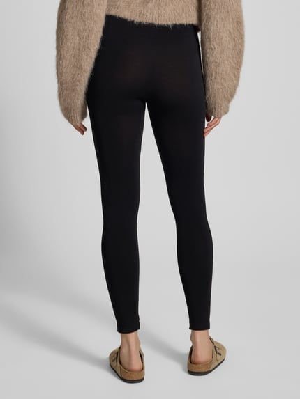Frauenmodel trägt schwarze Leggings aus Viskose-Mix im nahtlosen Design Modell 'BAMBOO' von MAGIC Bodyfashion, enganliegend, elastischer Bund, unifarben, feuchtigkeitsabsorbierend, Ganzkörperansicht Rückansicht.