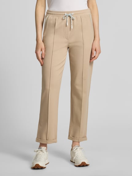 Frauenmodel trägt Straight Fit Stoffhose mit Ziernähten von Marc Cain aus Elastischer Baumwoll-Mix mit Modal-Anteil in Beige, Nahaufnahme Unterkörper, sichtbarer Tunnelzug-Bund und fixierte Beinabschlüsse, 7/8-Länge, Bundweite 39 cm, Innenbeinlänge 70 cm.