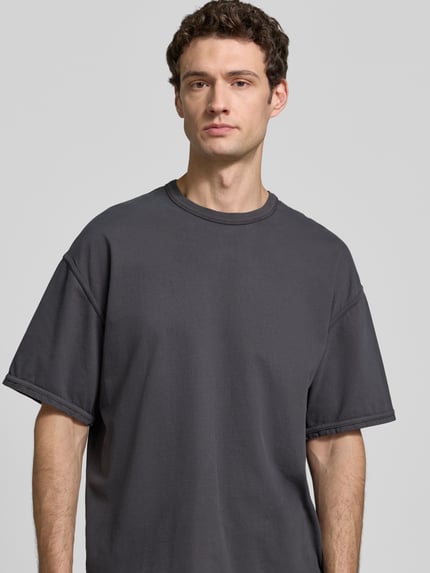 Męskimodel nosi t-shirt z bawełny w odcieniu grafitowym, krój relaxed fit, T-Shirt mit Rundhalsausschnitt Modell 'FAZY' von American Vintage, długość tyłu w rozmiarze M/L: 70 cm, okrągły dekolt, półzbliżenie przód.