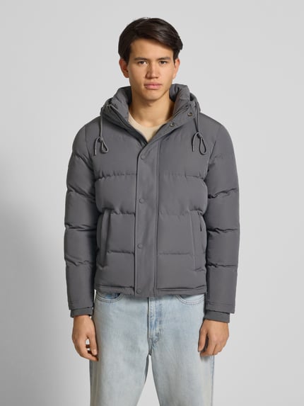 Männermodel trägt Steppjacke mit Eingrifftaschen Modell 'Everest' von Superdry in Grau, Regular Fit, Kapuze, Ganzkörperansicht von vorne, Rückenlänge bei Größe M 66 cm, Schulterbreite 48 cm, Brustweite 42 cm, Ärmellänge 70 cm.
