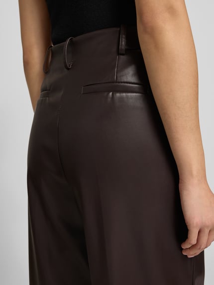 Vrouwenmodel draagt Stoffhose in Leder-Optik van Bash in donkerbruin met rechte snit en Franse zakken, detailopname heupen.