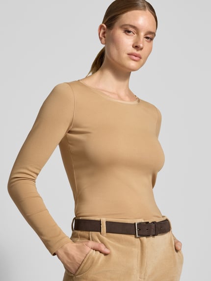 Frauenmodel trägt Slim Fit Langarmshirt aus Baumwoll-Mix von Marc Cain in Beige, glatte Struktur, U-Boot-Ausschnitt, Nahaufnahme Oberkörper. Markenlogo dezent erkennbar, elastischer Stoff.