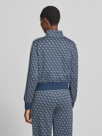 Frauenmodel trägt Regular Fit Sweatjacke mit Allover-Logo-Print von GUESS, blaues Muster, elastische Abschlüsse, Ganzkörperansicht Rückansicht.