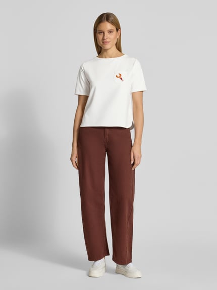 Vrouwenmodel draagt T-shirt met borstzak en motief van More & More in witte viscosemix met stretch, regular fit, ronde hals, parels, ruglengte maat 36: 54 cm. Volledige lichaamsopname van voren.