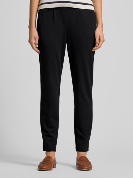 Frauenmodel trägt Easy Pants mit Bundfalten von TOM TAILOR in Schwarz, Viskosemischung mit Stretch-Anteil, schmal zulaufende Beine, französische Eingrifftaschen, Ganzkörperansicht von vorne.