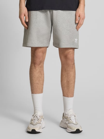 Männermodel trägt Regular Fit Sweatpants mit Logo-Stitching von adidas Originals in Grau, Baumwoll-Mix, Knielänge, Nahaufnahme Vorderansicht.