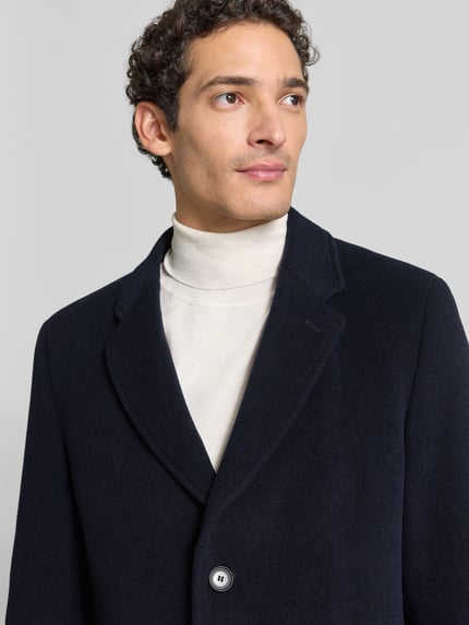 Männermodel trägt Mantel mit herausnehmbarer Steppweste von BOSS in Unifarbe, strukturierter Webware, Nahaufnahme Oberkörper.