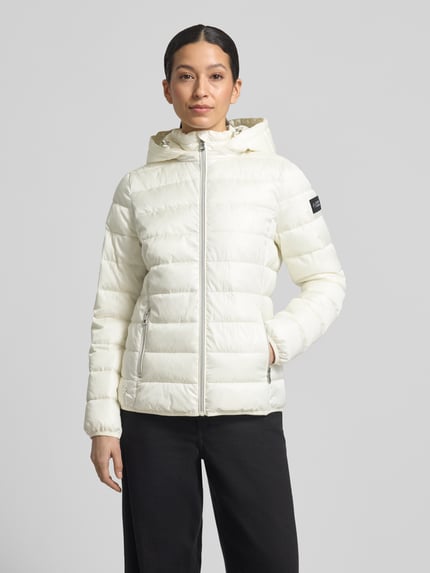 Frauenmodel trägt Regular Fit Steppjacke mit Kapuze von NAUTGÅRD in Weiß, gesteppt, verdeckter Reißverschluss, Ganzkörperansicht von vorne.