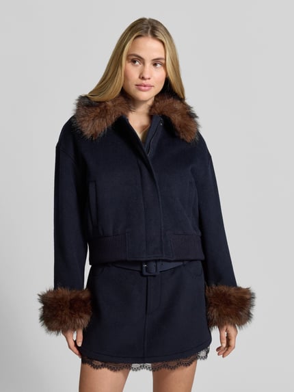 Frauenmodel trägt Wolljacke aus Woll-Viskose-Mix von Self-Portrait in Dunkelblau mit Kunstfellbesatz an Kragen und Ärmelenden, Regular Fit, Abdeckleiste und Eingrifftaschen, Vorderansicht, Nahaufnahme Oberkörper.