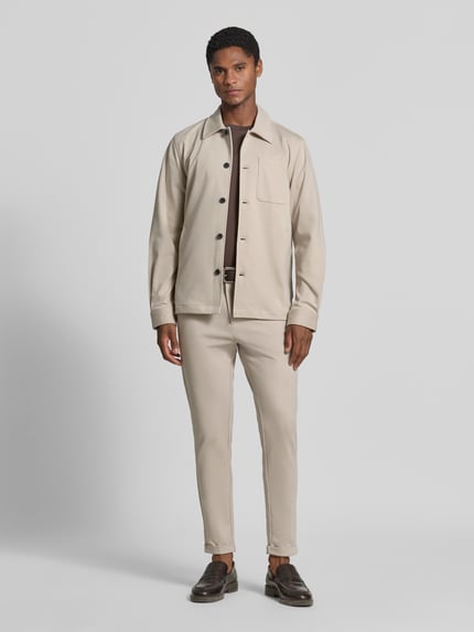 Männermodel trägt Slim Fit Stoffhose mit umgeschlagenen Hosenbeinen von Lindbergh in Beige, elastischer Material-Mix, Ganzkörperansicht von vorne.