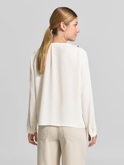 Frauenmodel trägt Regular Fit Bluse mit Volants von Marc Cain in Creme mit V-Ausschnitt und Label-Detail, Ganzkörperansicht Rückansicht.