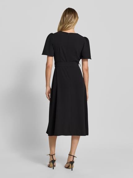 Frauenmodel trägt Cocktailkleid mit Gürtel und Rundhalsausschnitt von Rinascimento in Schwarz, Material-Mix mit Stretch-Anteil, Taillierter Schnitt, Midikleid, Rückseitiger Reißverschluss, Rückenlänge bei Größe S 36 cm, Brustweite 40 cm, Ärmellänge 28 cm, Ganzkörperansicht Rückansicht.