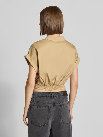 Vrouwenmodel draagt Cropped Hemdbluse aus reiner Baumwolle mit Logo-Stitching van Karo Kauer in beige, elastische band, ruglengte maat S 45 cm, zuiver katoen, korte mouwen, overhemdkraag, knoopsluiting, rugaanzicht.