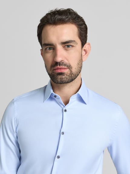 Männermodel trägt Super Slim Fit Business Hemd aus Baumwolle mit Kentkragen von Jake*s, hellblau, Nahaufnahme Oberkörper, glatte Struktur.