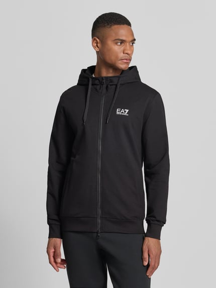 Männermodel trägt Slim Fit Sweatjacke mit Kapuze von EA7 Emporio Armani in Schwarz, Baumwoll-Mix, Logo-Print, Eingrifftaschen, Ganzkörperansicht von vorne.