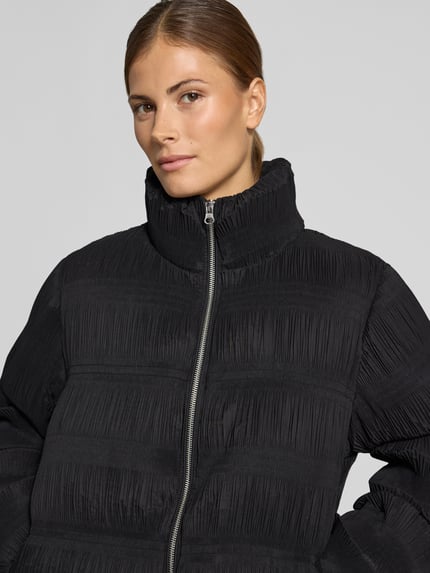 Frauenmodel trägt Steppjacke mit Zweiwege Reißverschluss von YAS, unifarben matt, strukturierte Oberfläche, Nahaufnahme Oberkörper.