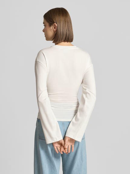 Kobiece model nosi bluzkę z długim rękawem z mieszanki bawełny, krój taliowany, okrągły dekolt, Model 'Paloma' od JJXX, długość tyłu w rozmiarze S: 57 cm, jasny kolor, gładka faktura, widok całej sylwetki z tyłu.
