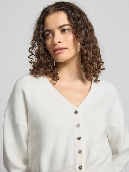 Kobiece modelka ma na sobie kardigan Regular Fit Cardigan mit Viskose-Anteil Modell 'Compact' od Topshop, mieszanka bawełny i wiskozy, imitacja dzianiny, dekolt w serek, kolor biały, zapięcie na guziki, długość tyłu 50 cm, długość rękawów 55 cm, krój regular fit; zbliżenie na górną część ciała.