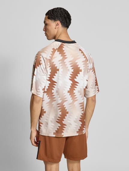 Mężczyzna model nosi Regular Fit T-Shirt mit Allover-Muster von adidas Sportswear, efekt: wzór na całej powierzchni, krój regular fit, nadruk z logo, okrągły dekolt, krótki rękaw, Ganzkörperansicht Rückansicht.