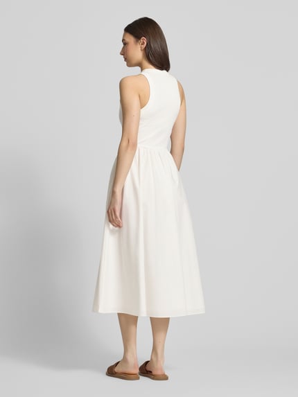 Frauenmodel trägt Midikleid aus reiner Baumwolle von Tommy Jeans in Unifarbe Weiß, ärmellos, A-Linie, Midi-Länge, Ganzkörperansicht Rückansicht.
