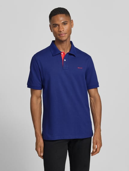 Männermodel trägt Regular Fit Poloshirt mit Logo-Stitching von Gant in Blau, Baumwoll-Mix, Polokragen, Kurzarm, Ganzkörperansicht von vorne.