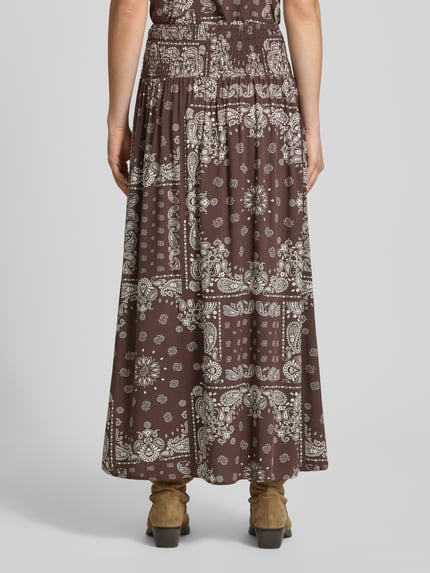 Vrouwenmodel draagt bruine uitgespreide maxi rok van pure viscose model 'SAKI AMBEL' van Only met wit paisley motief, dames maxi-rok, ganzonderaanzicht achteraan.