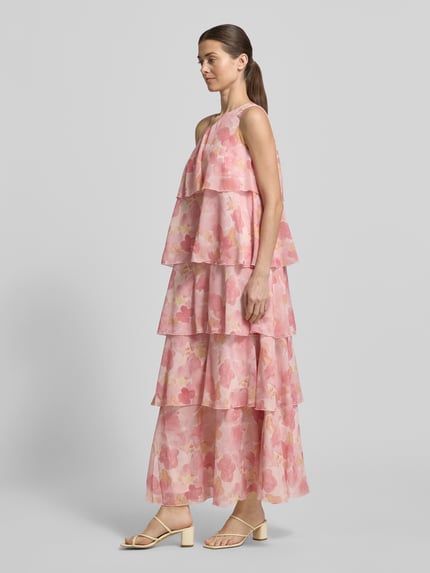 Frauenmodel trägt Ausgestelltes Maxikleid mit Rüschendetail Modell 'FELICIA' von Vero Moda aus rosa Chiffon mit floralem Allover-Muster, Maxi-Länge, One-Shoulder-Träger, asymmetrischem Ausschnitt, Volantsaum und blickdichtem Unterkleid, Ganzkörperansicht von vorne.