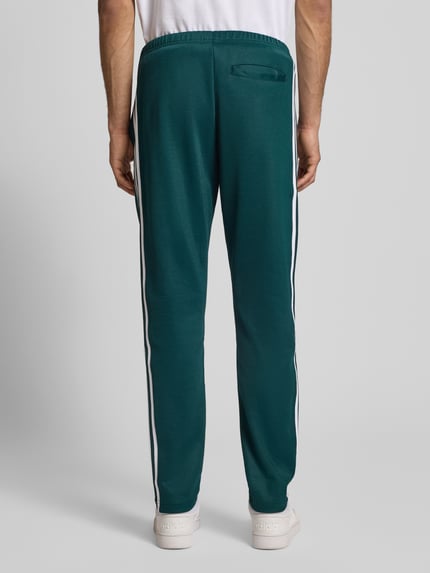 Männermodel trägt Sweatpants mit elastischem Bund van adidas Originals in donkergroen met witte strepen, katoenmengsel, losse pasvorm, zichtbare achterzak, volledige achterkantaanzicht.