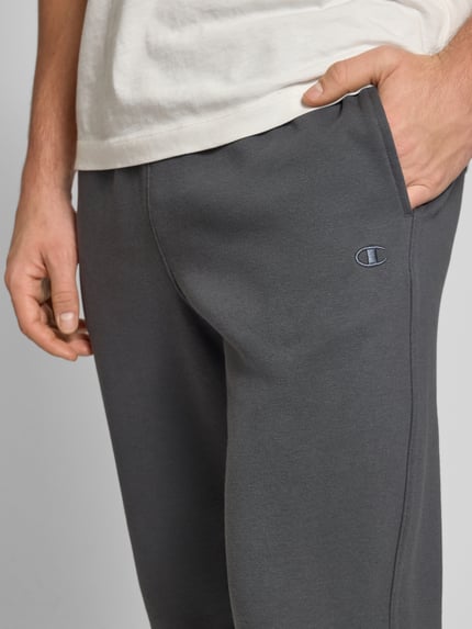 Męski model nosi Sweatpants mit elastischem Bund od CHAMPION, kolor ciemnoszary, luźny krój, bawełniany miks, zbliżenie na biodra.