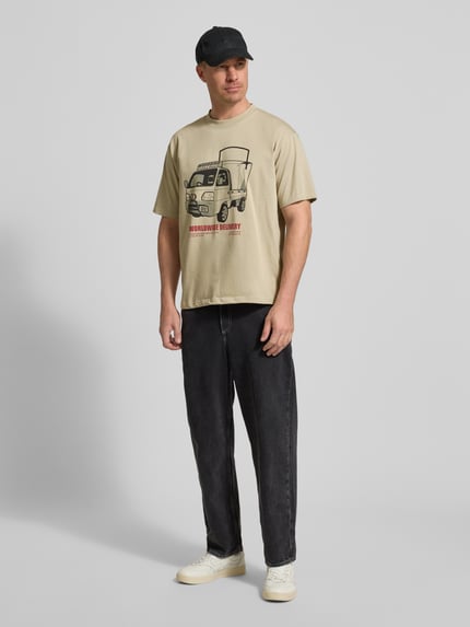 Männermodel trägt T-Shirt mit Motiv-Print Modell 'Baine' von WOODBIRD in Beige, Regular Fit, Bio-Baumwolle, Ganzkörperansicht von vorne.