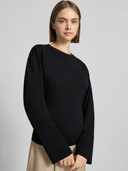 Kobiece modelka ma na sobie czarną bluzkę z długim rękawem z mieszanki bawełny, krój taliowany, okrągły dekolt, Model 'Paloma' od JJXX, długość tyłu w rozmiarze S: 57 cm, zdjęcie całej sylwetki z przodu.