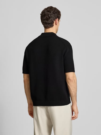 Männermodel trägt Relaxed Fit Poloshirt aus reiner Baumwolle Modell 'DANE' von SELECTED HOMME in Schwarz, Strickoptik, Ganzkörperansicht Rückansicht