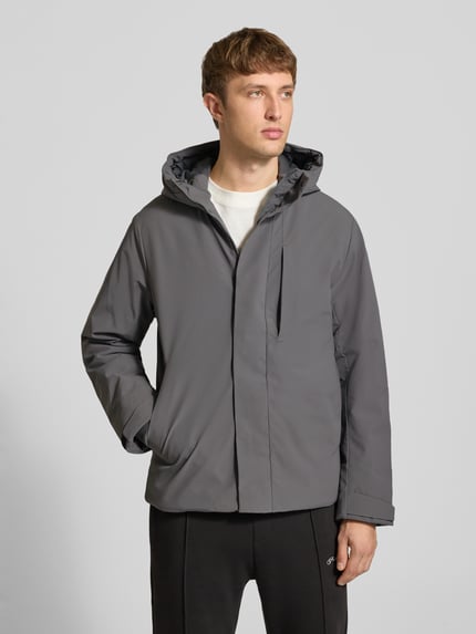 Mężczyzna nosi kurtkę z kapturem Jacke mit verdecktem Reißverschluss Modell 'KEEN' od JACK & JONES, krój regular fit, szara, Patki przy mankietach, Długość tyłu w rozmiarze M: 72 cm, szerokość ramion w rozmiarze M: 49 cm, szerokość klatki piersiowej w rozmiarze M: 60 cm, długość rękawów w rozmiarze M: 68 cm, widok całej sylwetki z przodu