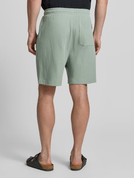 Männermodel trägt Relaxed Fit Sweatshorts aus reiner Baumwolle von Tom Tailor Denim in Optik: Unifarben, Rippstrick, Ganzkörperansicht Rückansicht.